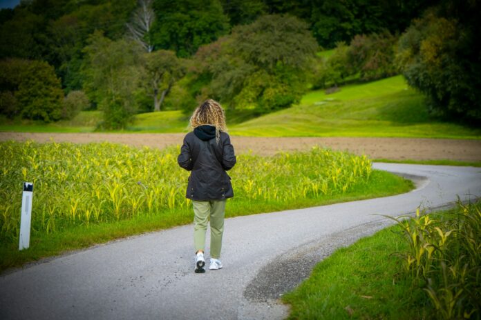 Photo by Scorn Pion Woman walking on a winding road through fields.