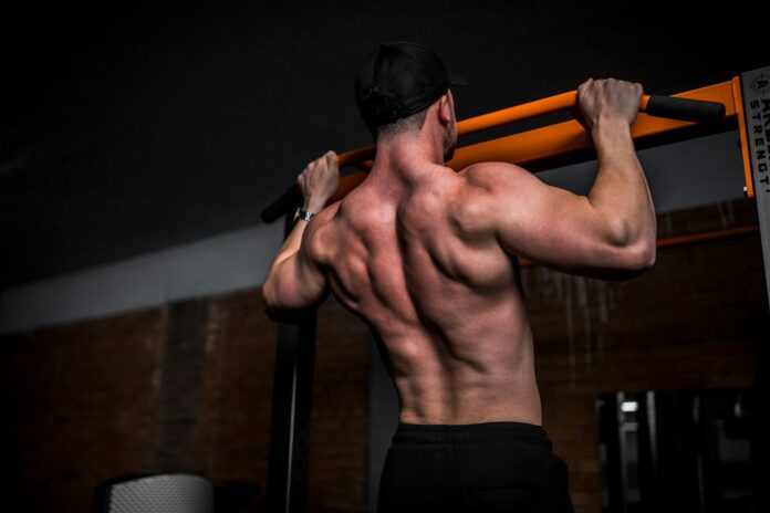 Photo by Anastase Maragos topless man in black shorts holding orange bar